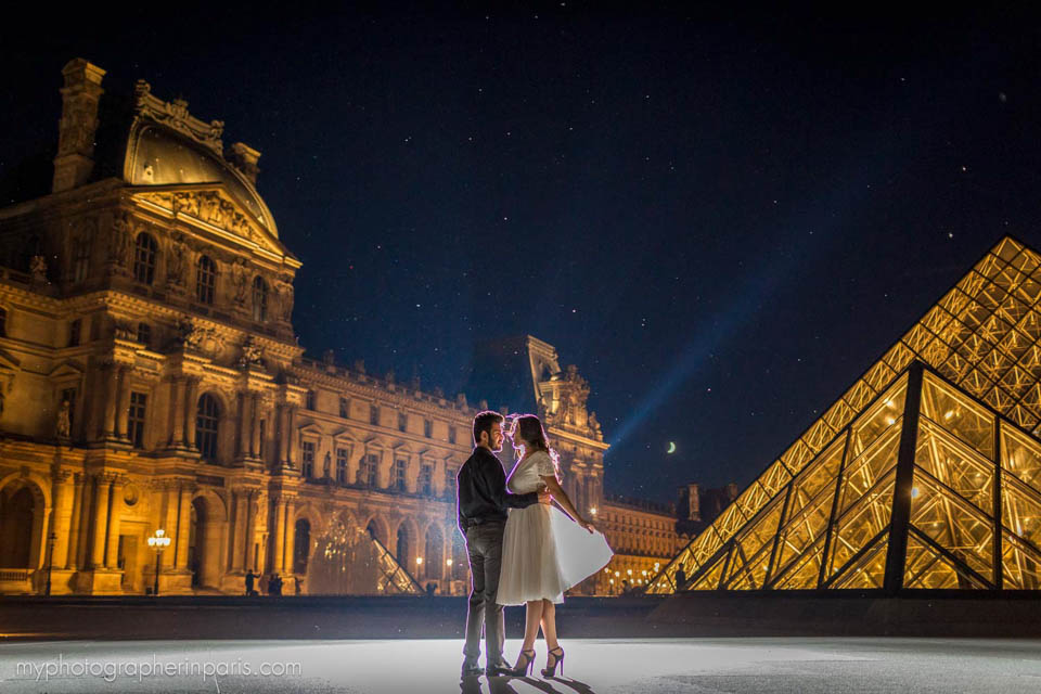 Couple dancing at the Louvre Museum at night with the Eiffel Tower in the distance