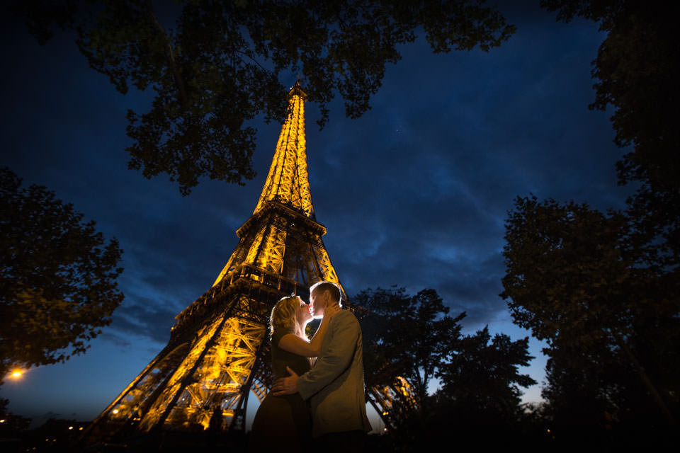 Couple kissing at dusk at the foot of the Eiffel Tower