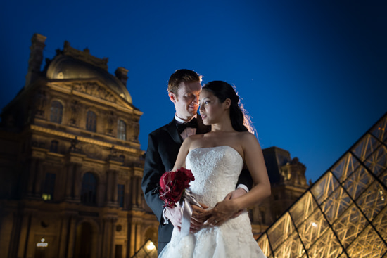 A groom embracing his bride at night at the Louvre Museum in Paris