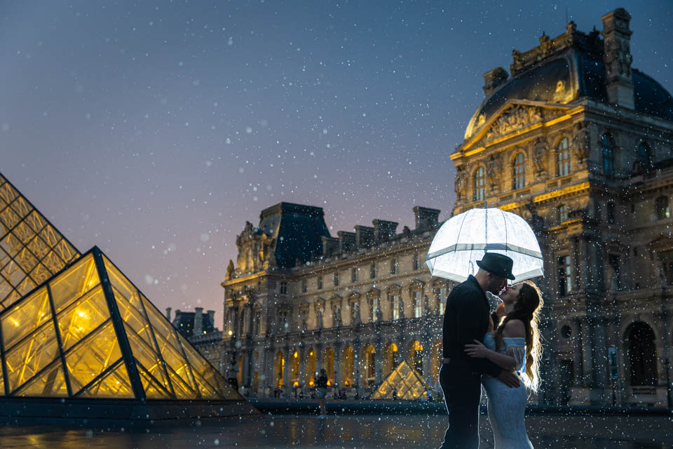 night-photoshoot-in-paris Couple kissing under an umbrella at the Louvre Museum.