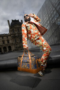 Man posing in a suit at the Louvre Museum with a bag and sunglasses